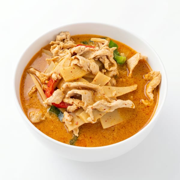Red curry with sliced chicken, bamboo shoots, and bell peppers in a white bowl.