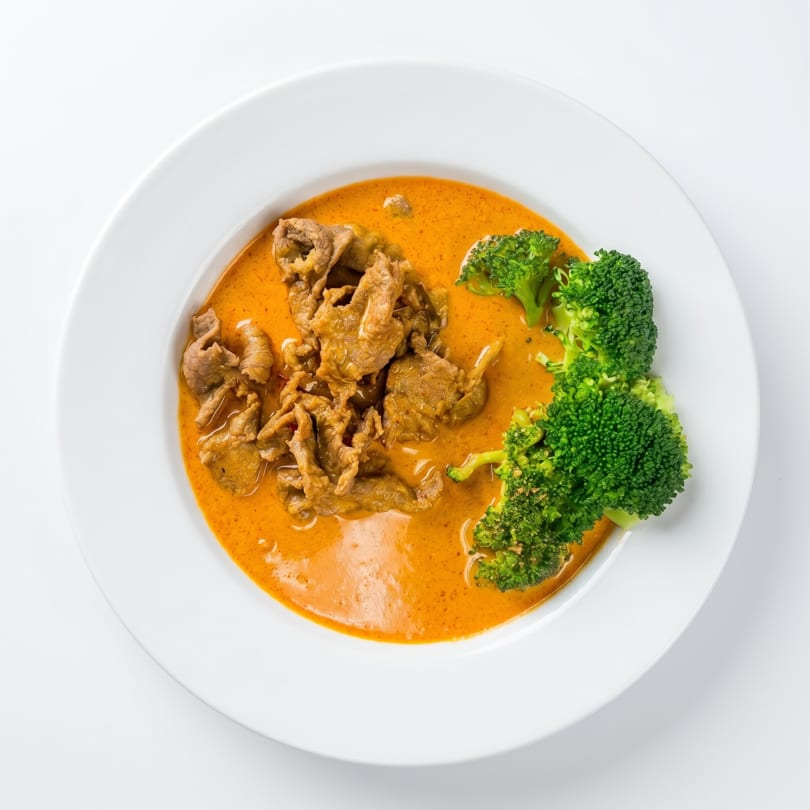 Beef curry with broccoli in a white bowl, against a white background.