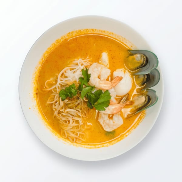 Spicy seafood noodle soup with shrimp, mussels, and cilantro in a white bowl.