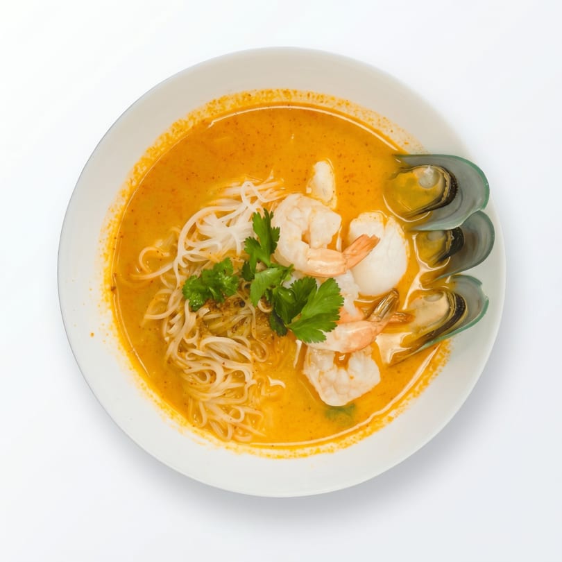 Spicy seafood noodle soup with shrimp, mussels, and cilantro in a white bowl.
