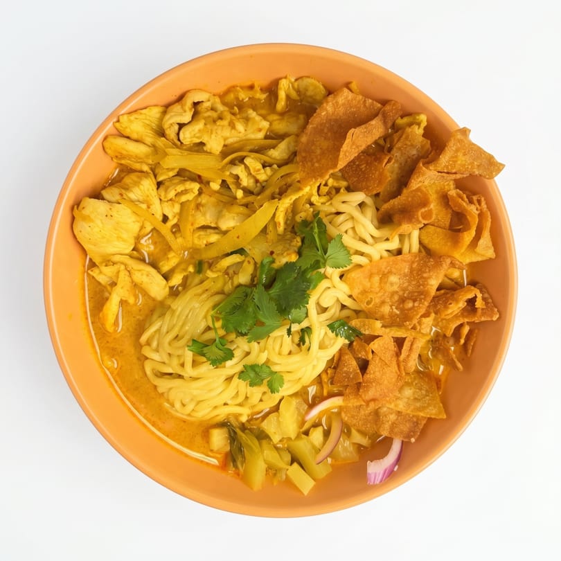 Overhead view of a bowl of Khao Soi, a Thai curry noodle soup with chicken and crispy wontons.